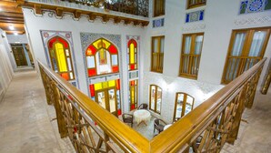 A multi-level interior with a central staircase, ornate stained glass windows, and a seating area with tables and chairs. - Hotel Volida Boutique (Bukhara)
