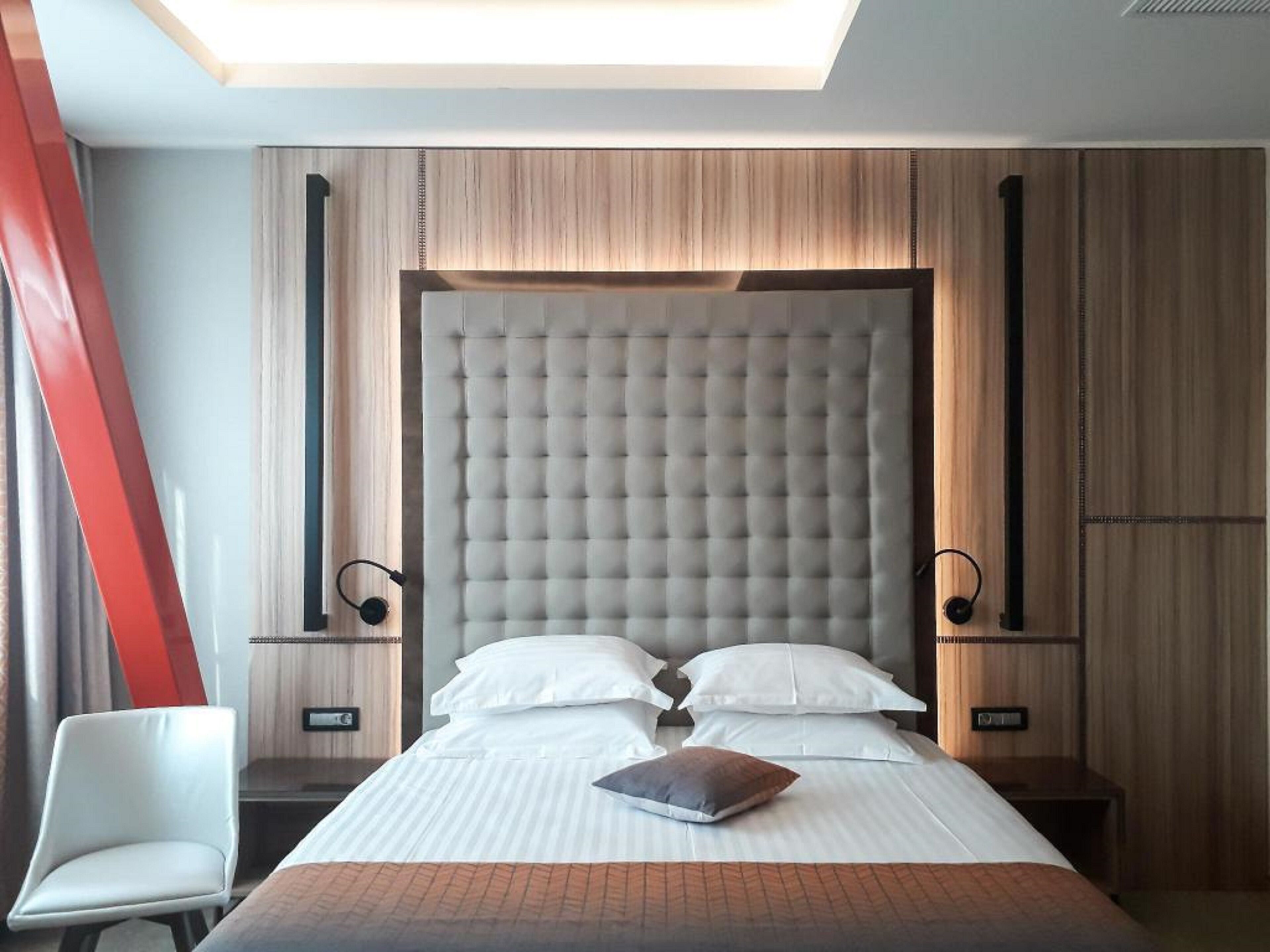 Una habitación de hotel moderna con una cama grande, dos mesitas de noche, una silla y un tragaluz.