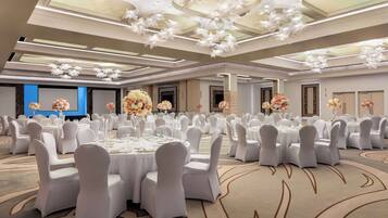 Een ruime balzaal met ronde tafels, witte stoelen en bloemdecoraties.