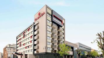 A modern hotel with a prominent 'RAMADA' sign, multiple balconies, and a clean, contemporary design.