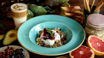 En morgenmadsopsætning med en skål granola toppet med yoghurt og bær, et glas kaffe samt frisk frugt som avocado og grapefrugt.