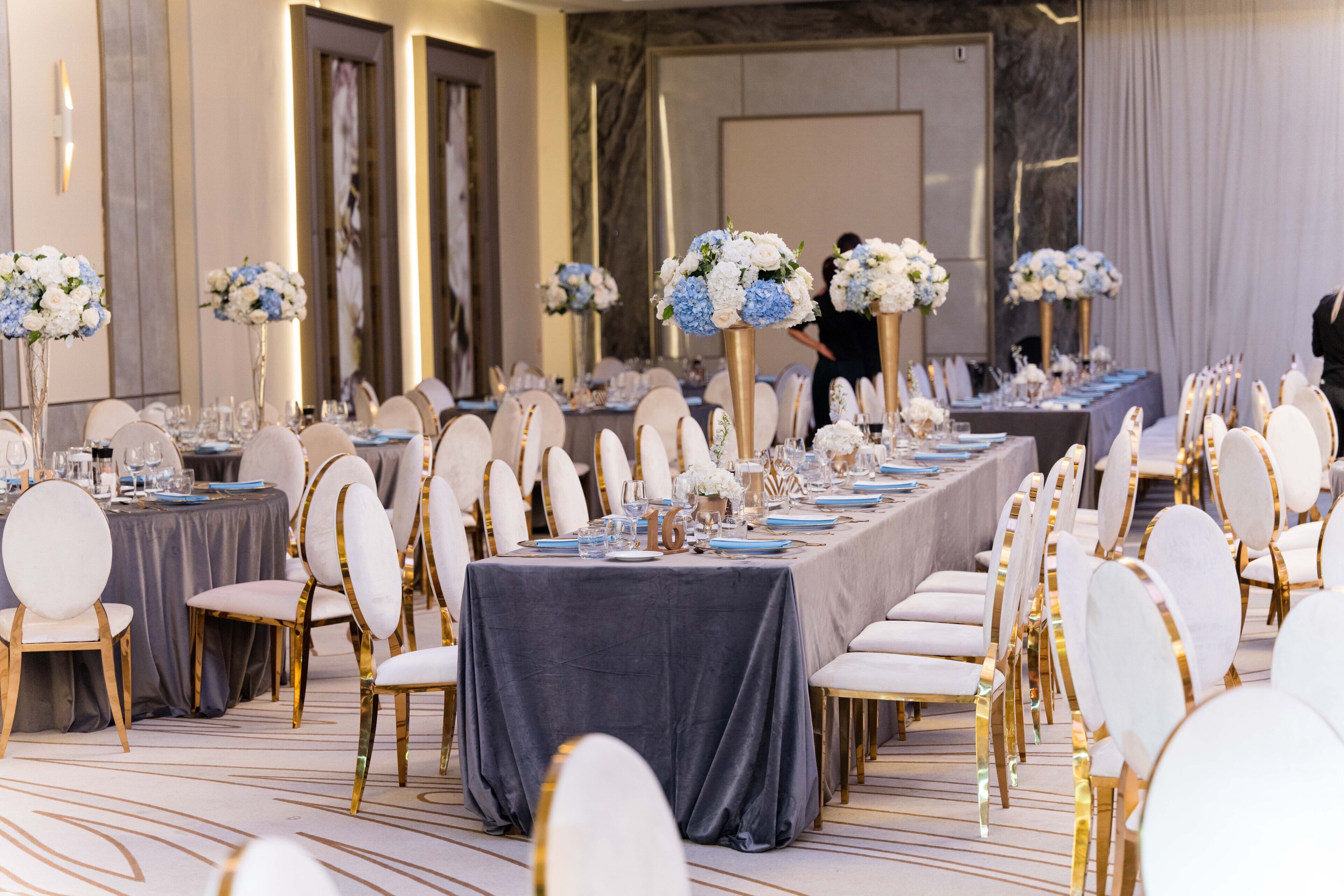 Une salle de banquet avec des tables rondes, des chaises blanches et des centres de table floraux bleus.