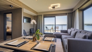 A modern hotel room with a dining area, a sofa, and a balcony with a view of the sea. - Golden Lakes Hotel (Froidchapelle)