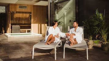 Dos personas sentadas en sillones de descanso en un espacio exterior moderno con pared de vidrio y piscina al fondo.