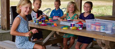 A group of children playing with toys at a wooden picnic table outdoors.