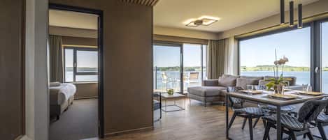 A modern hotel room with a large balcony, a dining area with a table and chairs, and a cozy sitting area with a sofa.