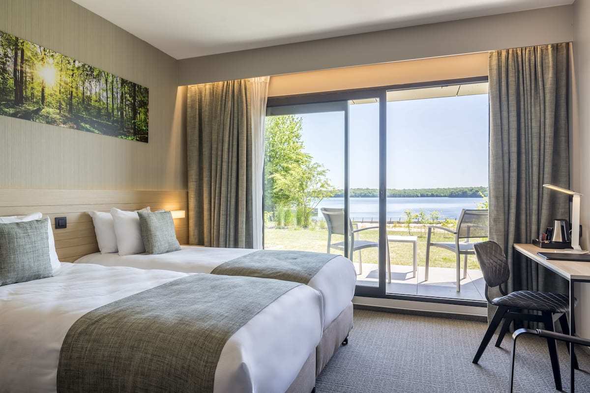 A hotel room with two beds, a desk, and a view of a lake.