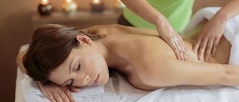 Iemand ontvangt een massage in een kamer met een wit bed en een kleine tafel met kaarsen op de achtergrond.