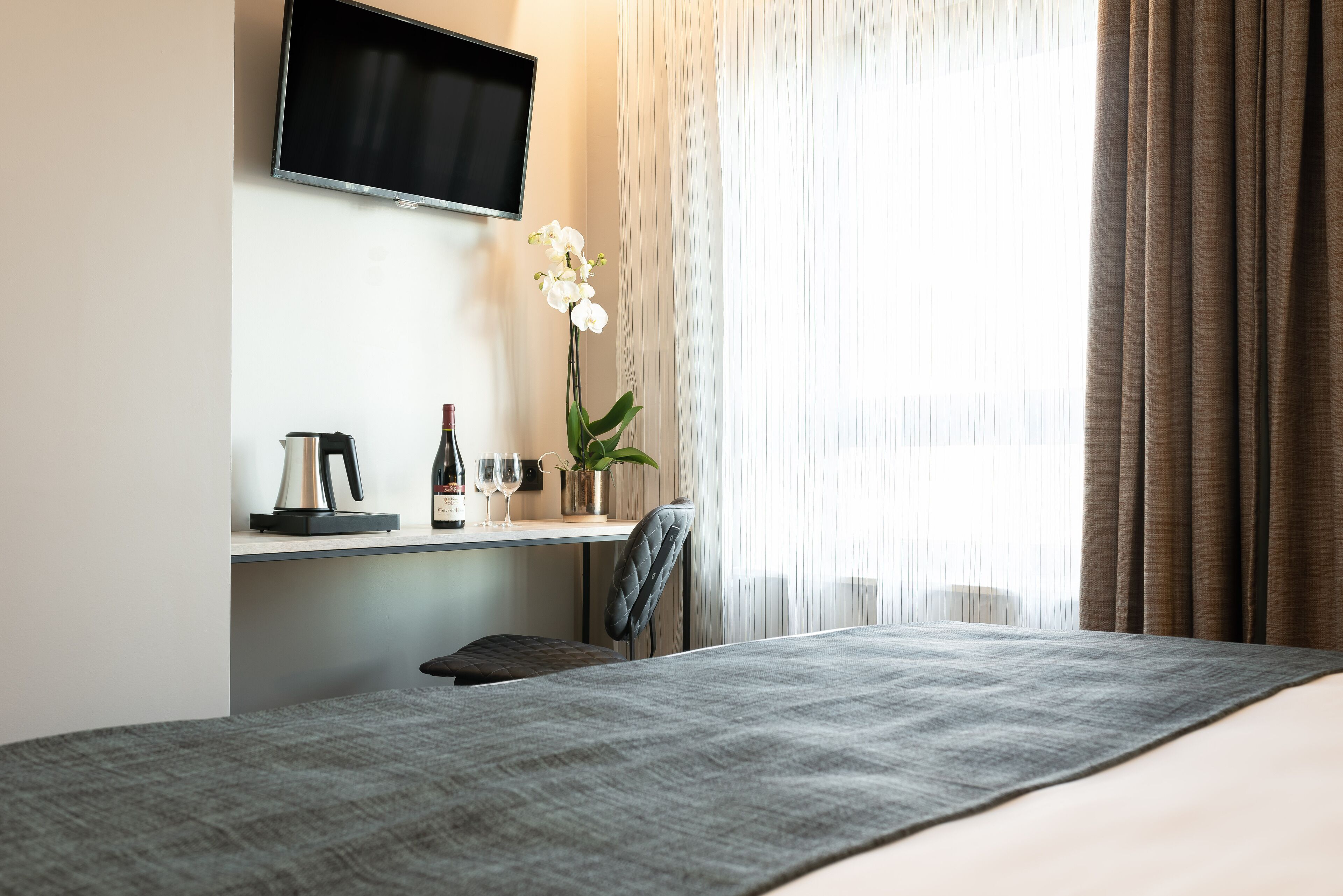 Ein Hotelzimmer mit Bett, Schreibtisch mit Wasserkocher, Weinglas und Topfpflanze.