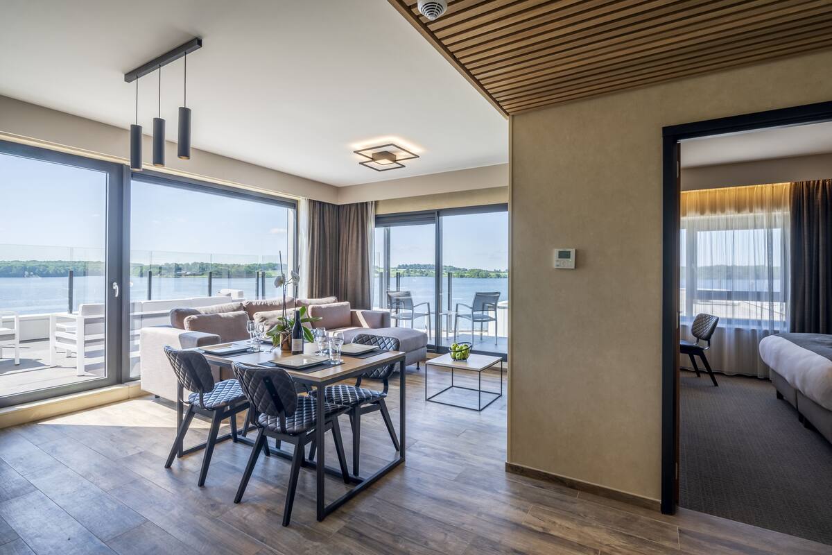 A modern hotel room with a balcony, a dining area, and a living space.