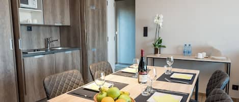 A modern dining area with a wooden table set for four, a basket of fruit, and a wine bottle.