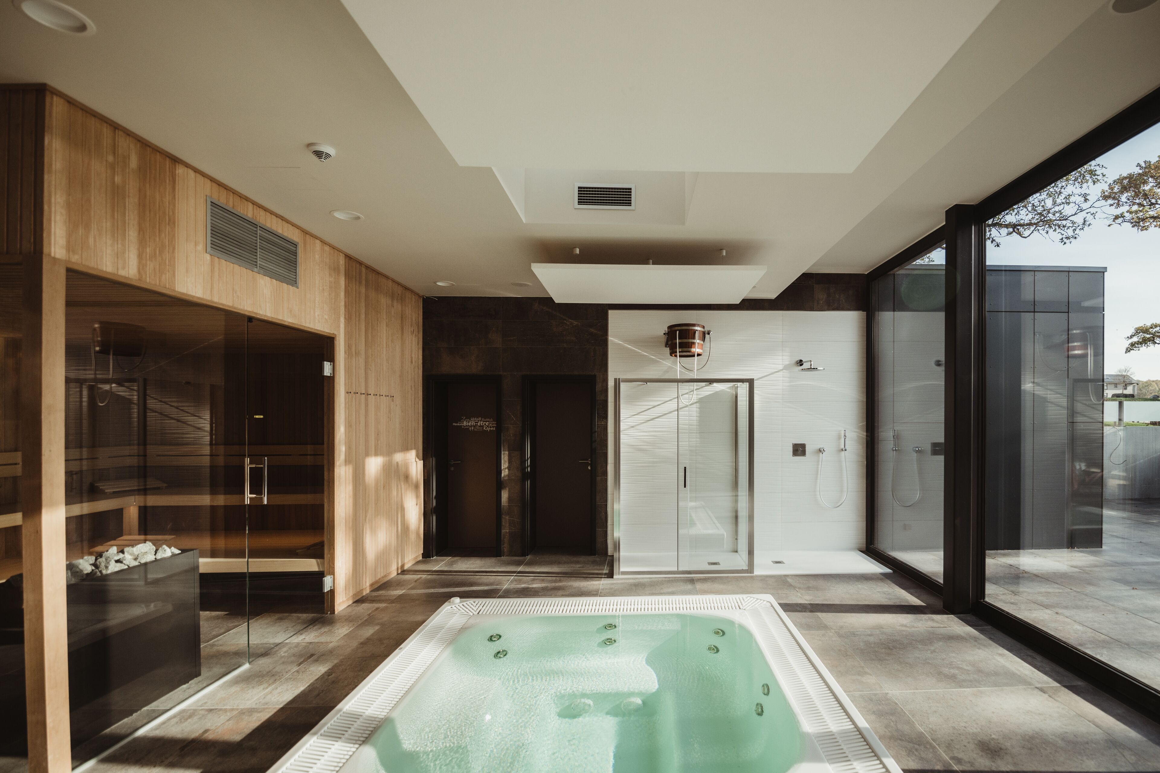 Ein moderner Wellnessbereich mit Whirlpool, Holzschränken und Glastüren.