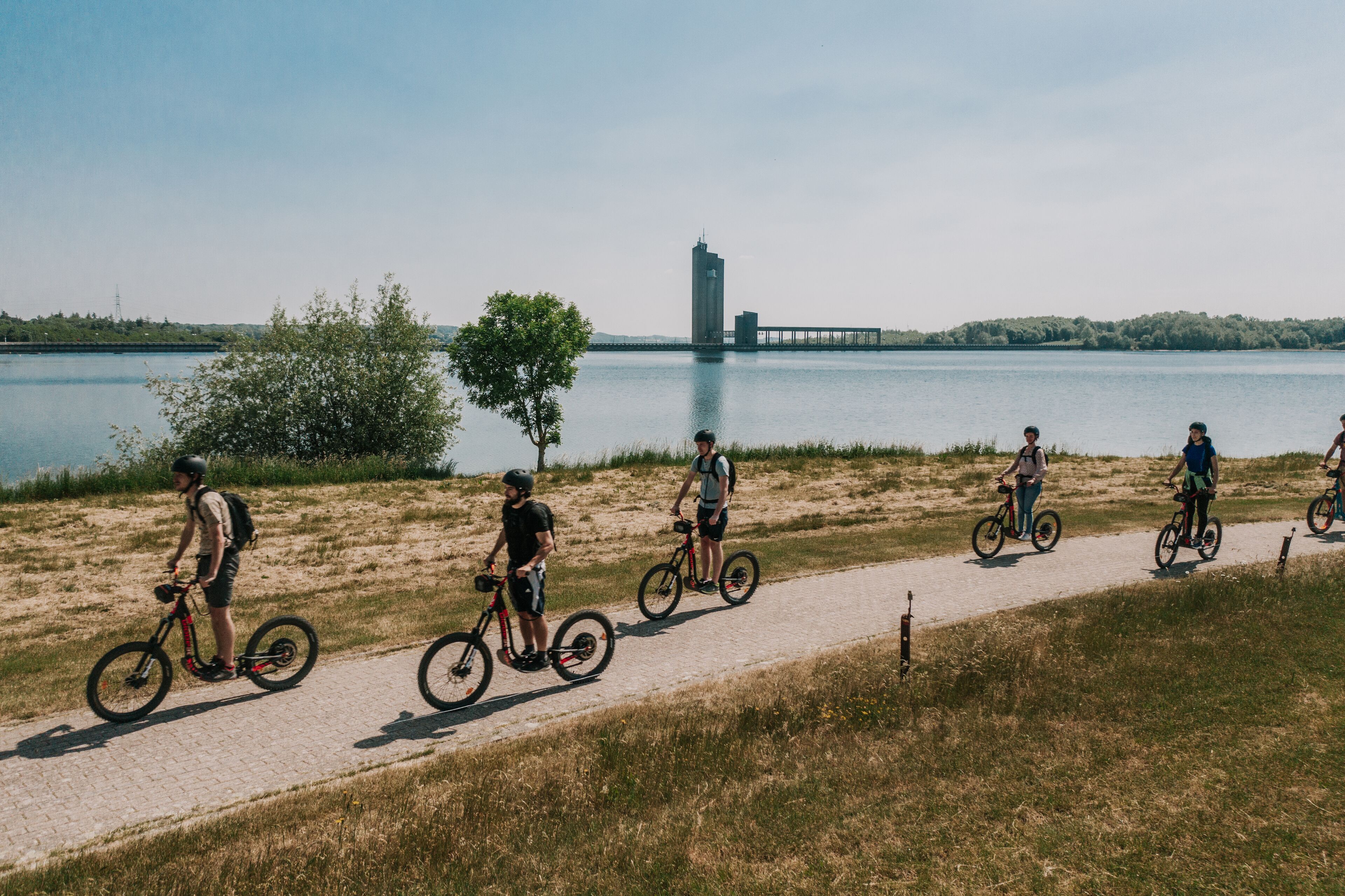 A paved path alongside a body of water with a bridge in the background.