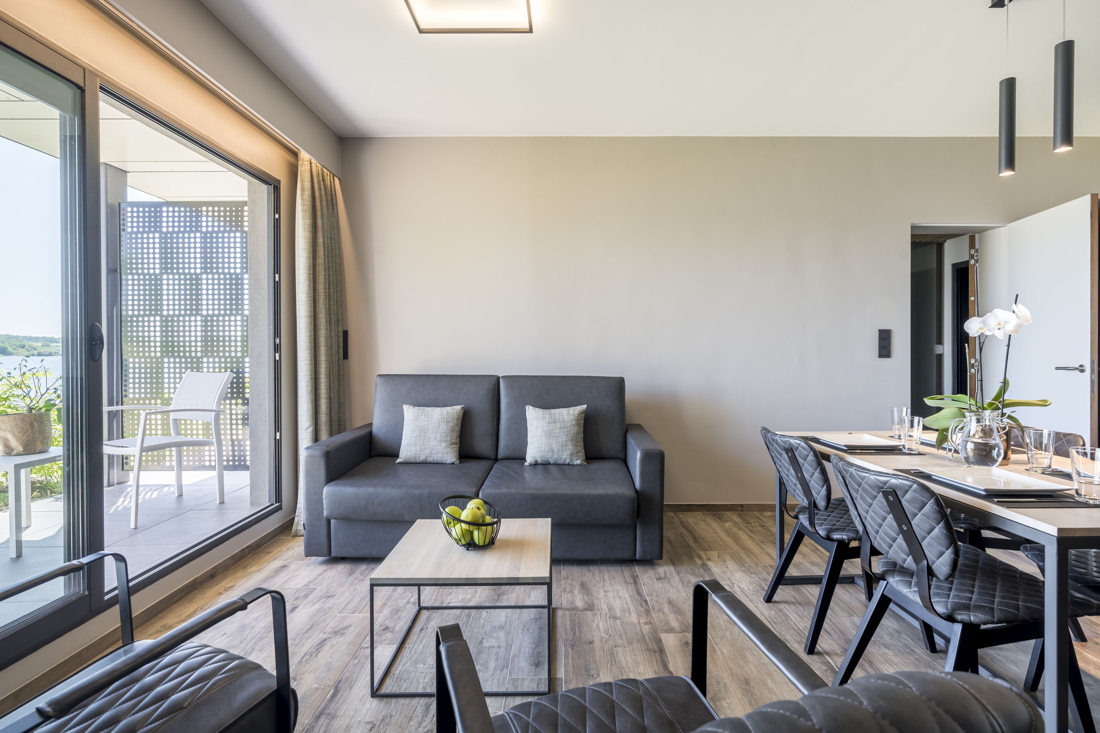 A modern living room with a grey sofa, a wooden coffee table, and a dining area with a table and chairs.