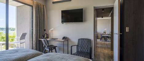 Habitación de hotel con dos camas, un escritorio con silla, televisión y balcón con una silla.