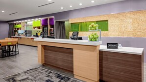 Zona de recepción de hotel con mostrador, quiosco digital y una exhibición de manzanas verdes.
