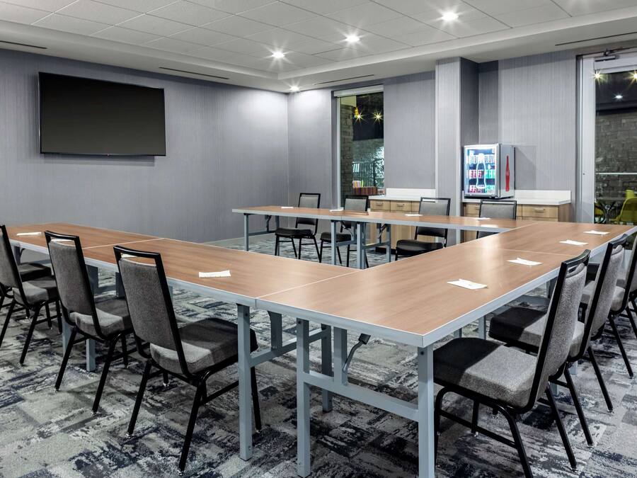 A conference room with a long table, chairs, a flat-screen TV, a refrigerator, and a vending machine.