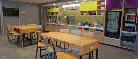 A restaurant with wooden tables and chairs, a counter with a coffee machine, and a refrigerator with beverages.