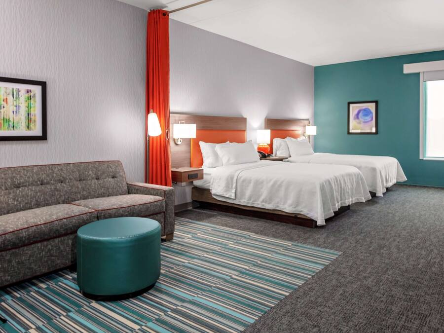 A hotel room with a sofa, two beds, a striped rug, and artwork on the walls.