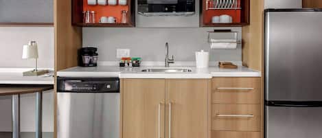 Una cocina compacta con lavavajillas, refrigerador de acero inoxidable y armarios de madera.
