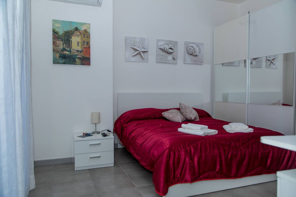 Un dormitorio moderno con una cama grande, una mesita de noche, un espejo y obras de arte en la pared.