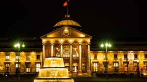 Un imposant bâtiment doté d’un dôme et de colonnes, une fontaine à l’avant et un drapeau au sommet.