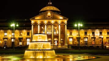 A grand building with a dome and columns, a fountain in front, and a flag on top.