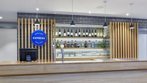 Un espace bar moderne avec un comptoir en bois, une enseigne indiquant « EXPRESS CAFE & BAR », et une variété de bouteilles et de verres exposés sur des étagères.