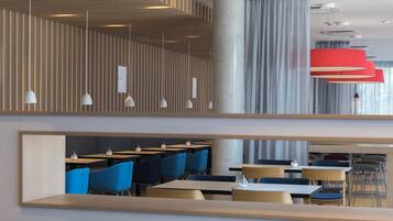 A modern interior with wooden slats on the walls, multiple tables and chairs, and pendant lighting.