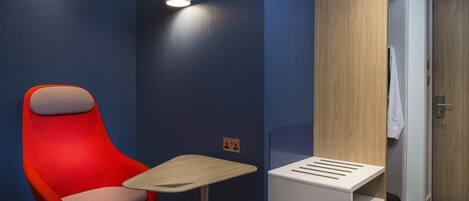 A modern hotel room with a red chair, a small table, and a wooden wardrobe.