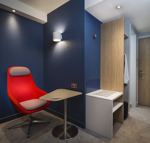 Une chambre d’hôtel moderne avec un fauteuil rouge, une petite table et une armoire en bois.