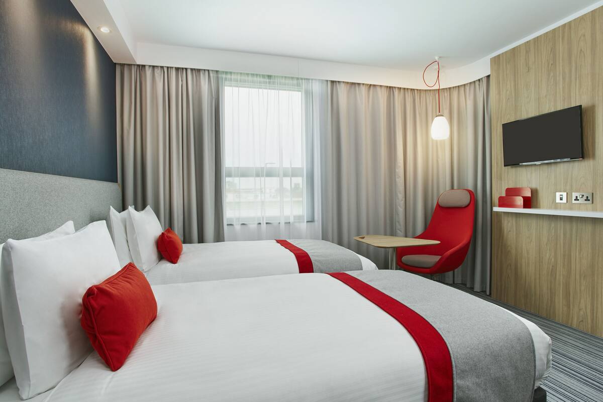 Una habitación de hotel con dos camas, un televisor, una silla roja y una mesita.