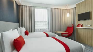 Una camera d'albergo con due letti, una televisione, una poltrona rossa e un tavolino.