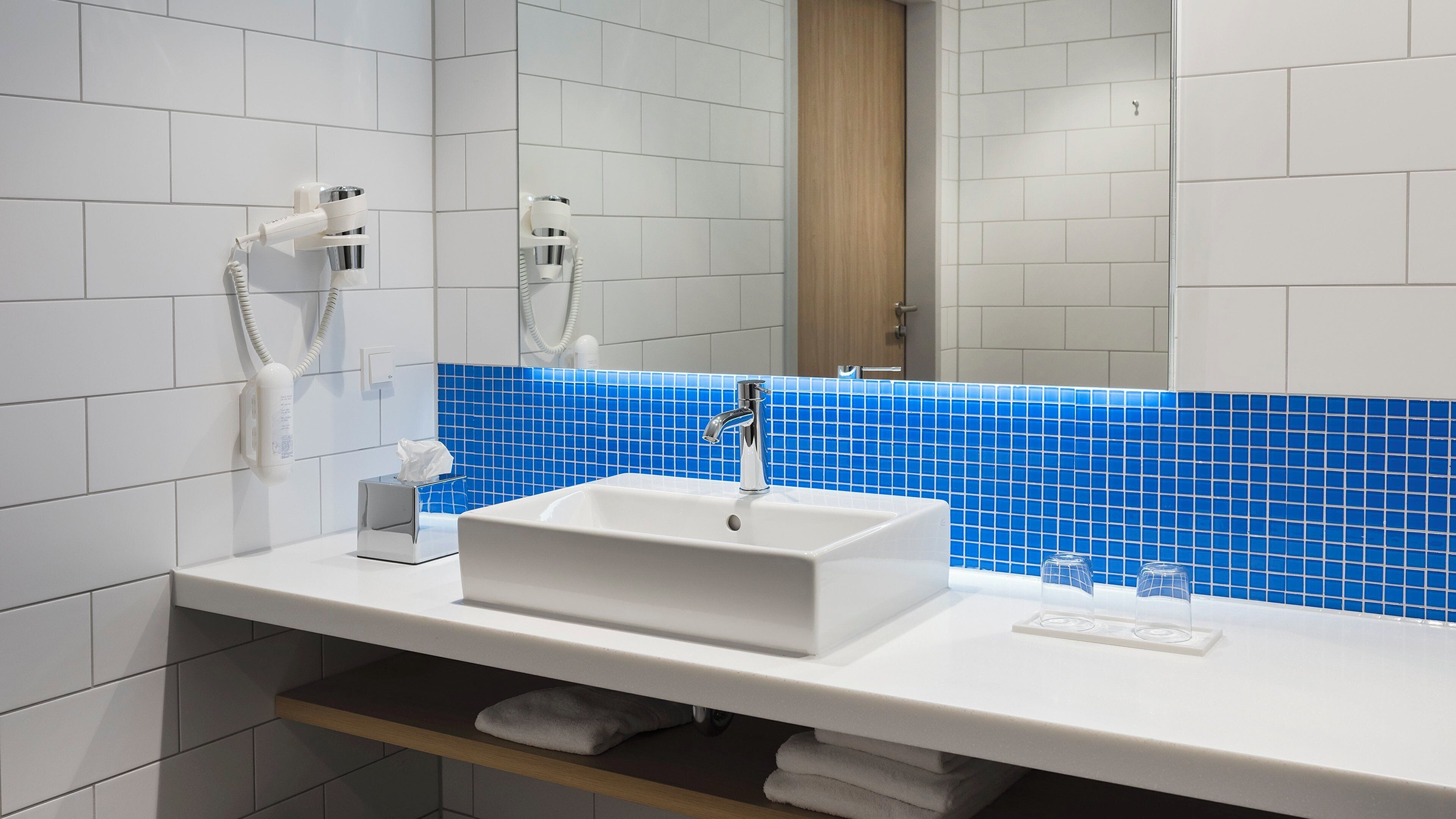 A bathroom with a white sink, a mirror, and a blue-tiled backsplash.