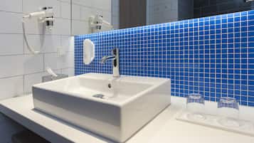 Een moderne badkamer met een wit wastafelmeubel, een blauwe tegelachtergrond en een handspiegel.