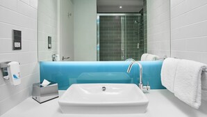 Une salle de bain moderne avec un lavabo blanc, un mur d’accent bleu, une douche en verre et une serviette blanche sur la droite.