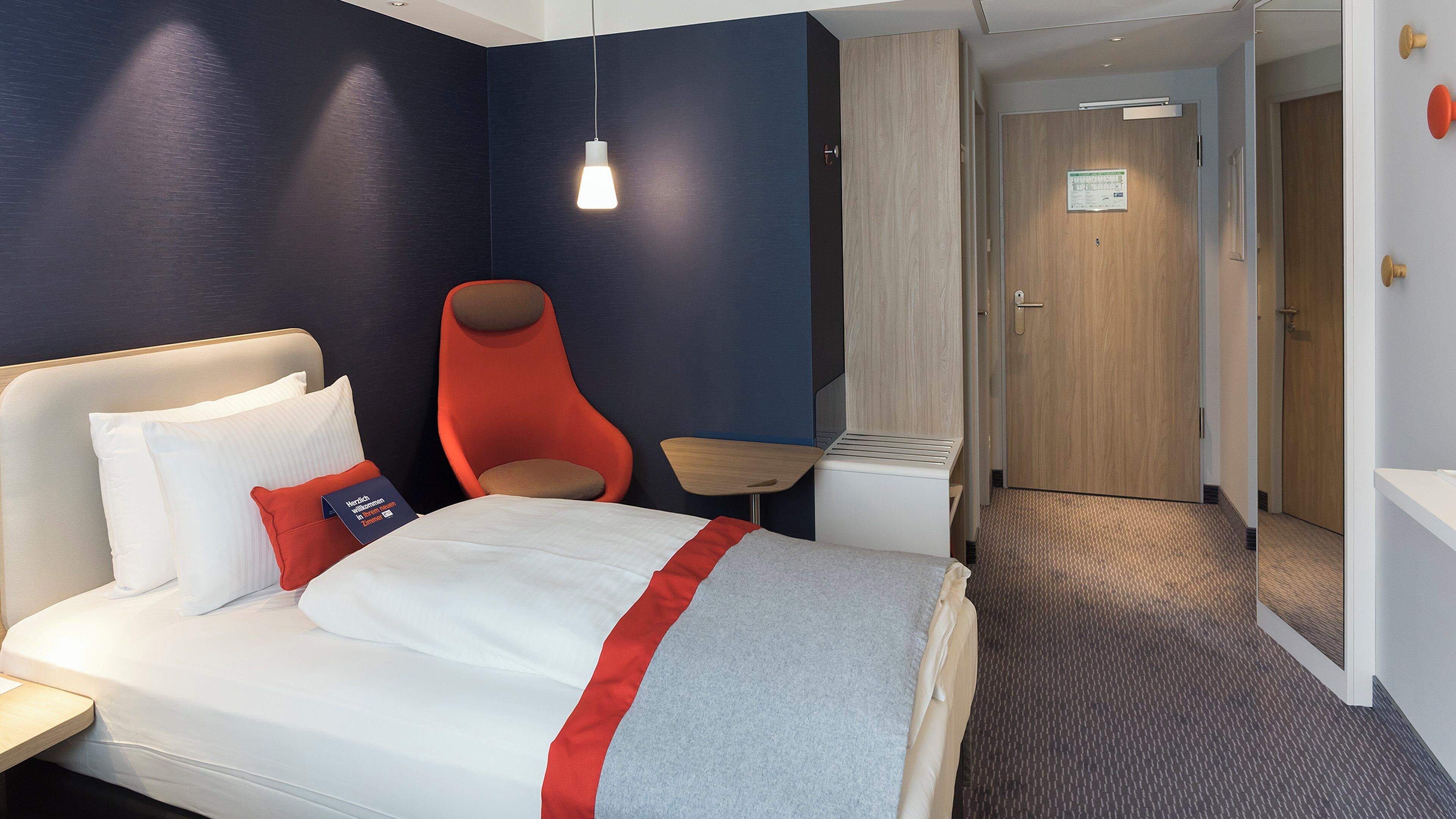 Ein Hotelzimmer mit einem Bett, einem Sessel, einem kleinen Tisch und einer Tür zu einem anderen Raum.