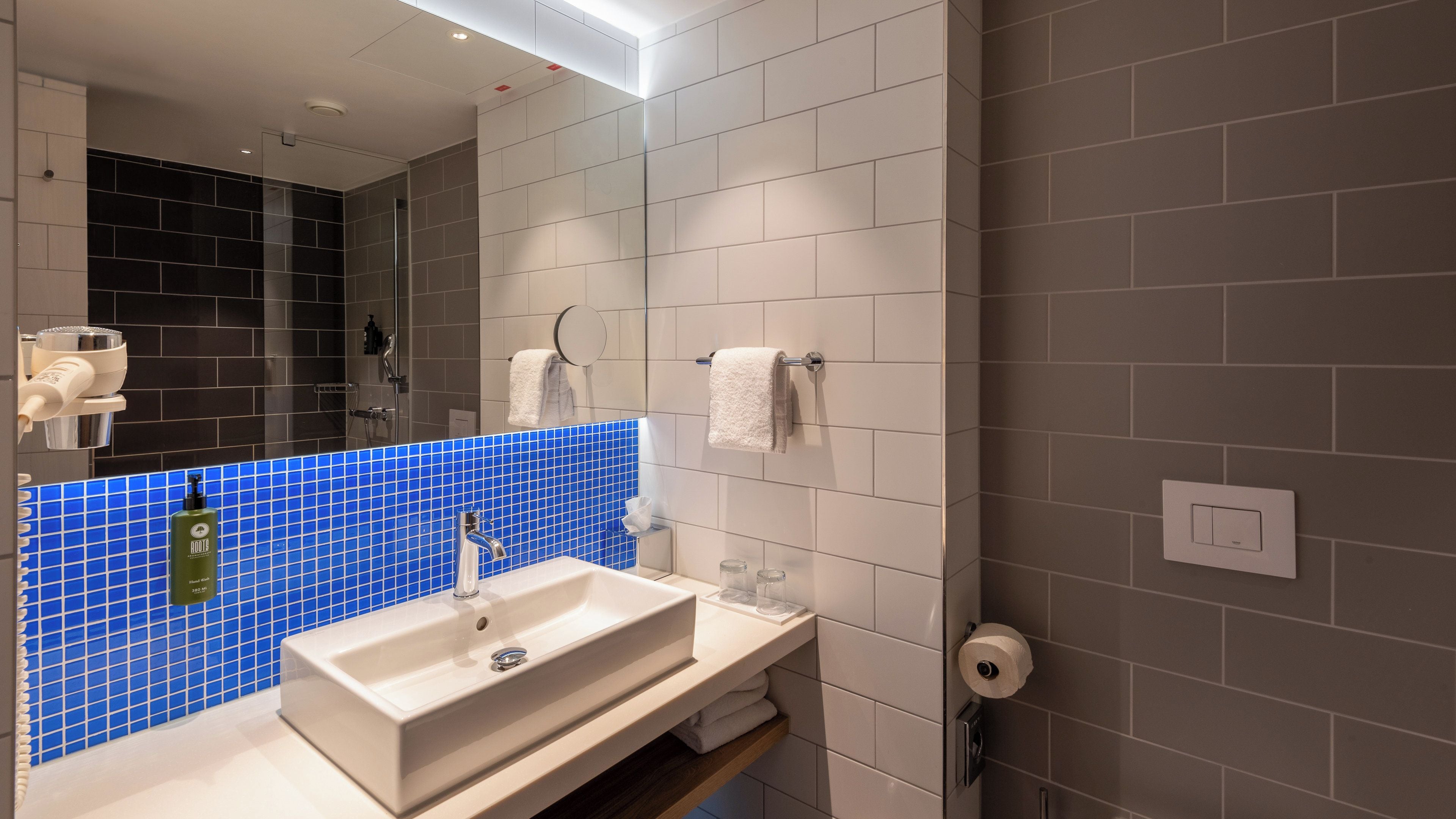 Ein modernes Badezimmer mit einem weißen Waschbecken, einer blauen Fliesenrückwand und einem Spiegel.