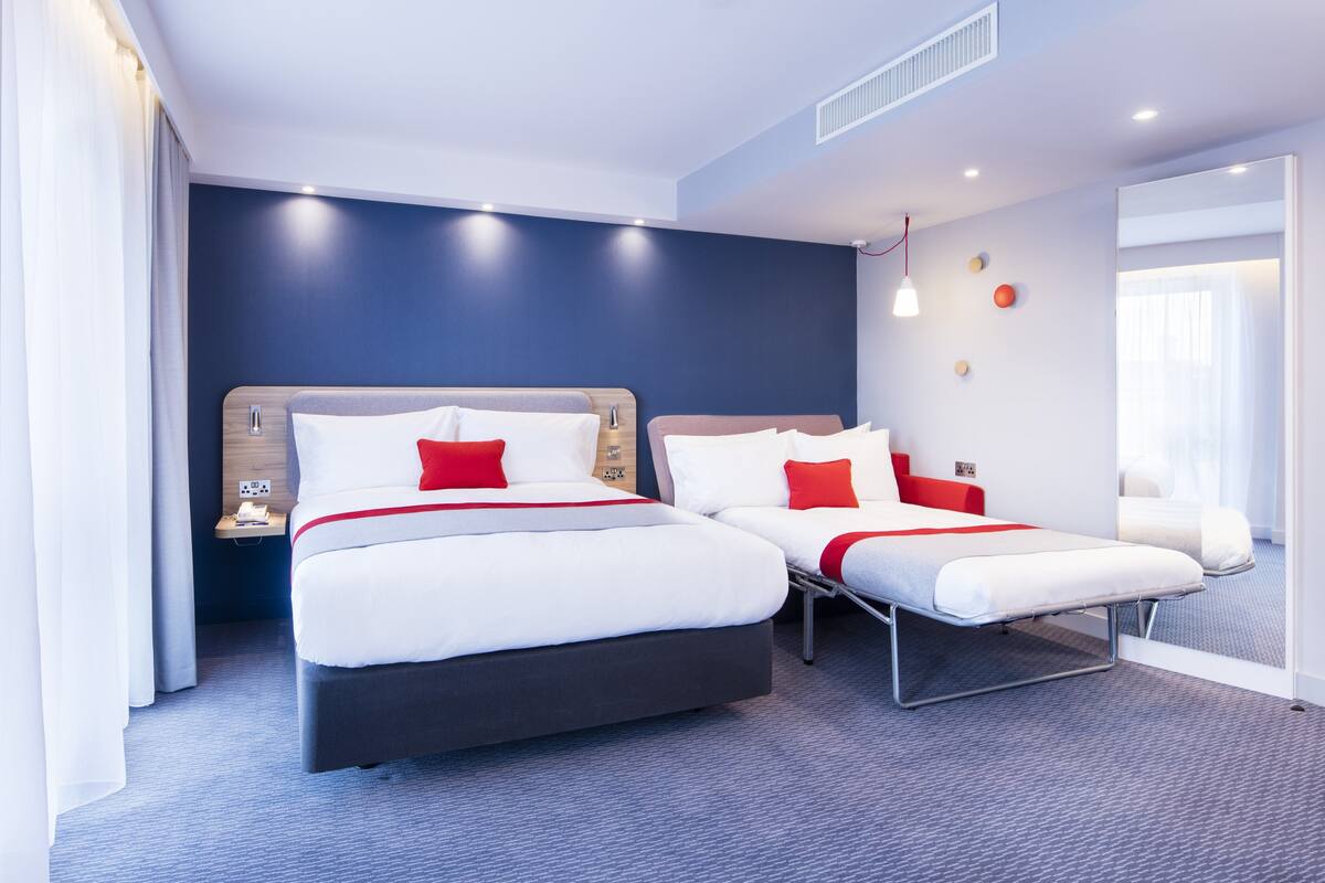 Habitación de hotel con dos camas, una mesita de noche y un ventanal grande.
