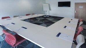 Une salle de conférence équipée d’une grande table, de chaises, d’un tableau blanc et d’une porte.