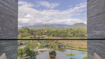 Un balcón con vistas a un jardín ajardinado, una piscina y una cascada.