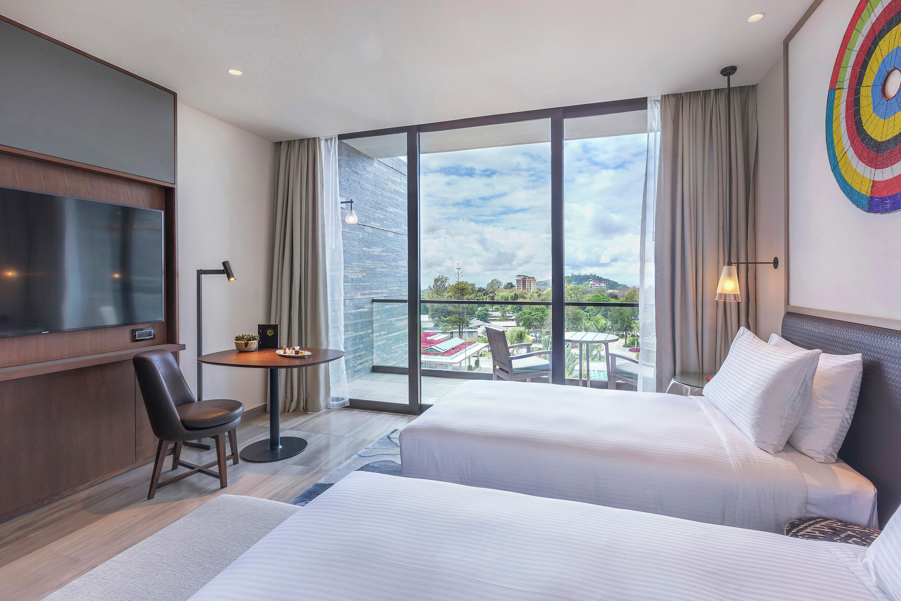 Habitación de hotel con cama, escritorio, silla, televisor y balcón con vistas.