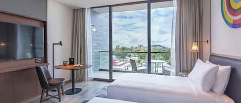 Habitación de hotel con cama, escritorio, silla, televisor y balcón con vistas.
