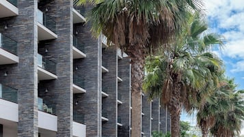Un edificio de varios pisos con balcones y un patio ajardinado con palmeras y plantas en macetas.