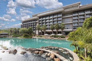 Un hotel con una piscina amplia, varios balcones y exuberante jardinería.