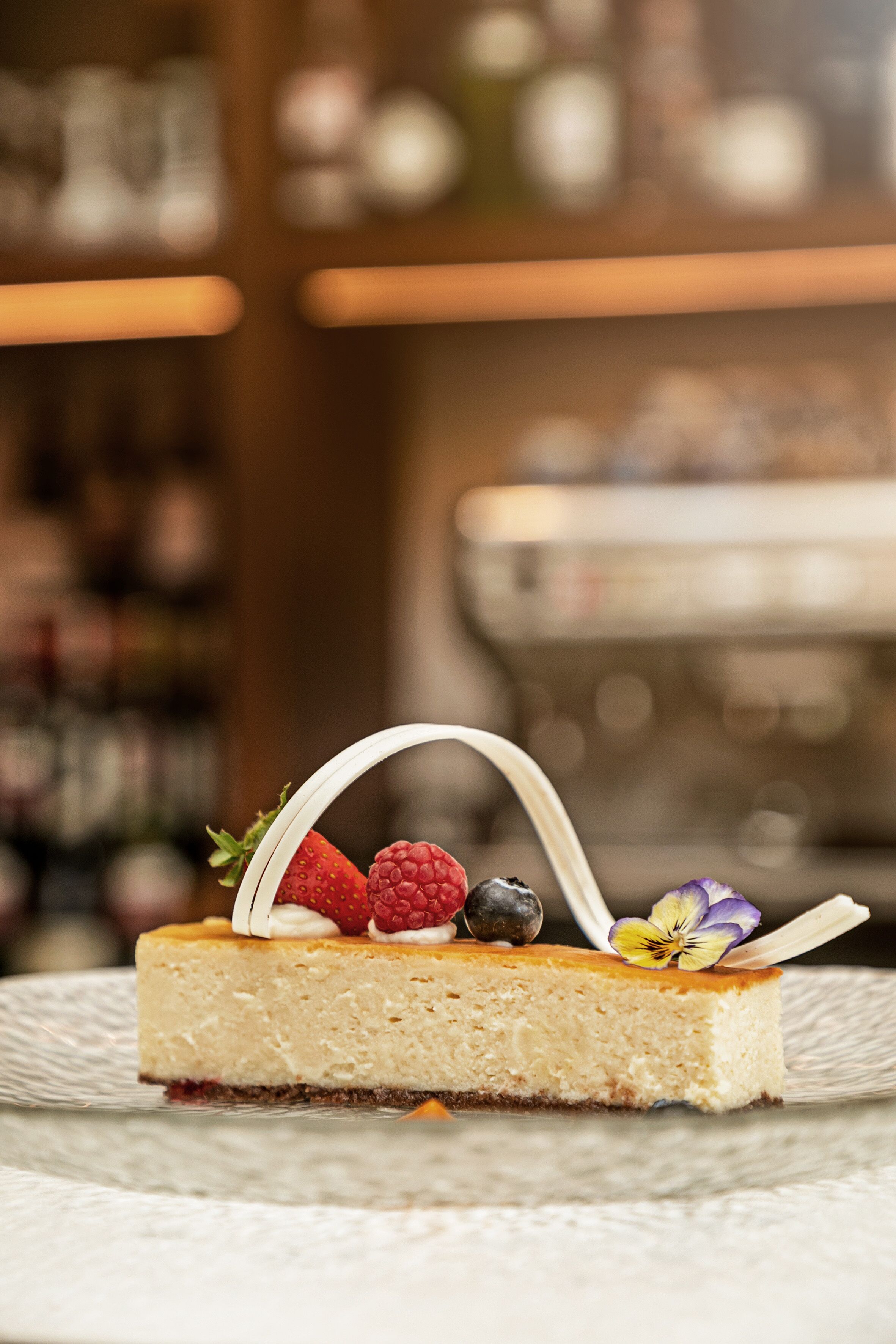 A slice of cheesecake with strawberries, raspberries, blueberries, and a flower on a white plate.