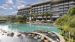 Un hotel moderno con una piscina grande, rodeado de palmeras y un jardín bien cuidado.