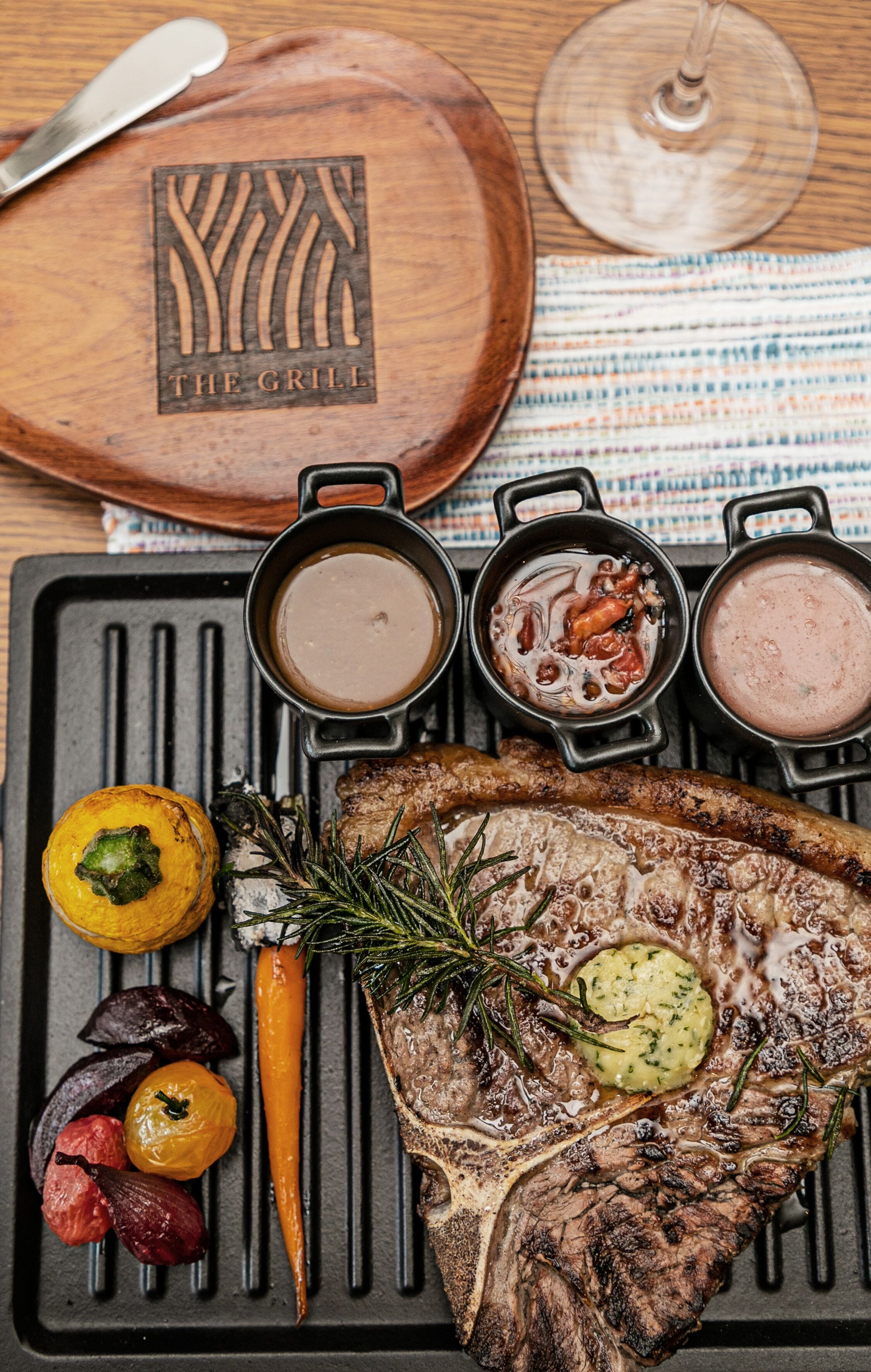 A grilled steak with vegetables and sauces on a grill pan.