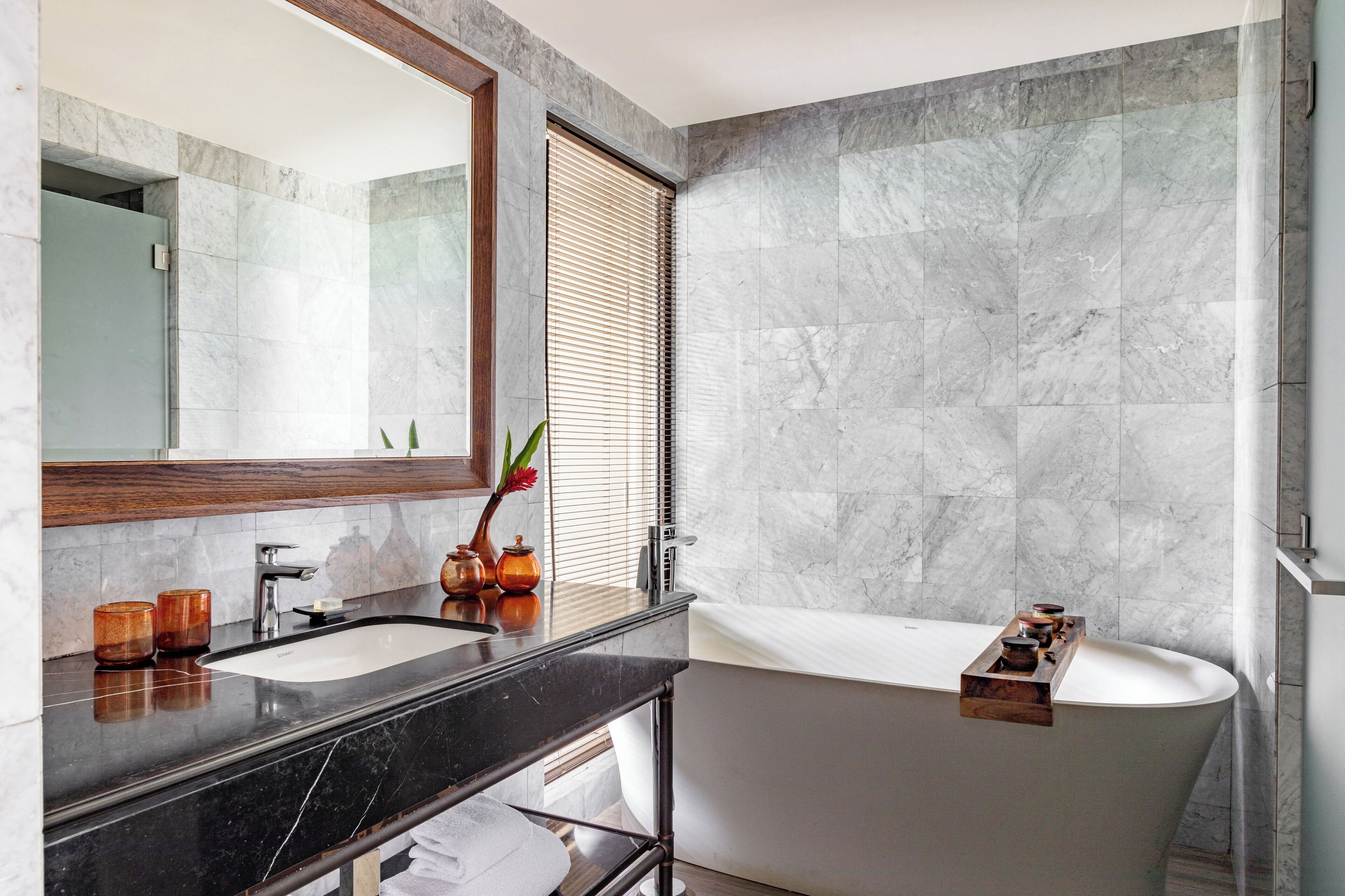A modern bathroom with a freestanding bathtub, a large mirror, and a marble wall.