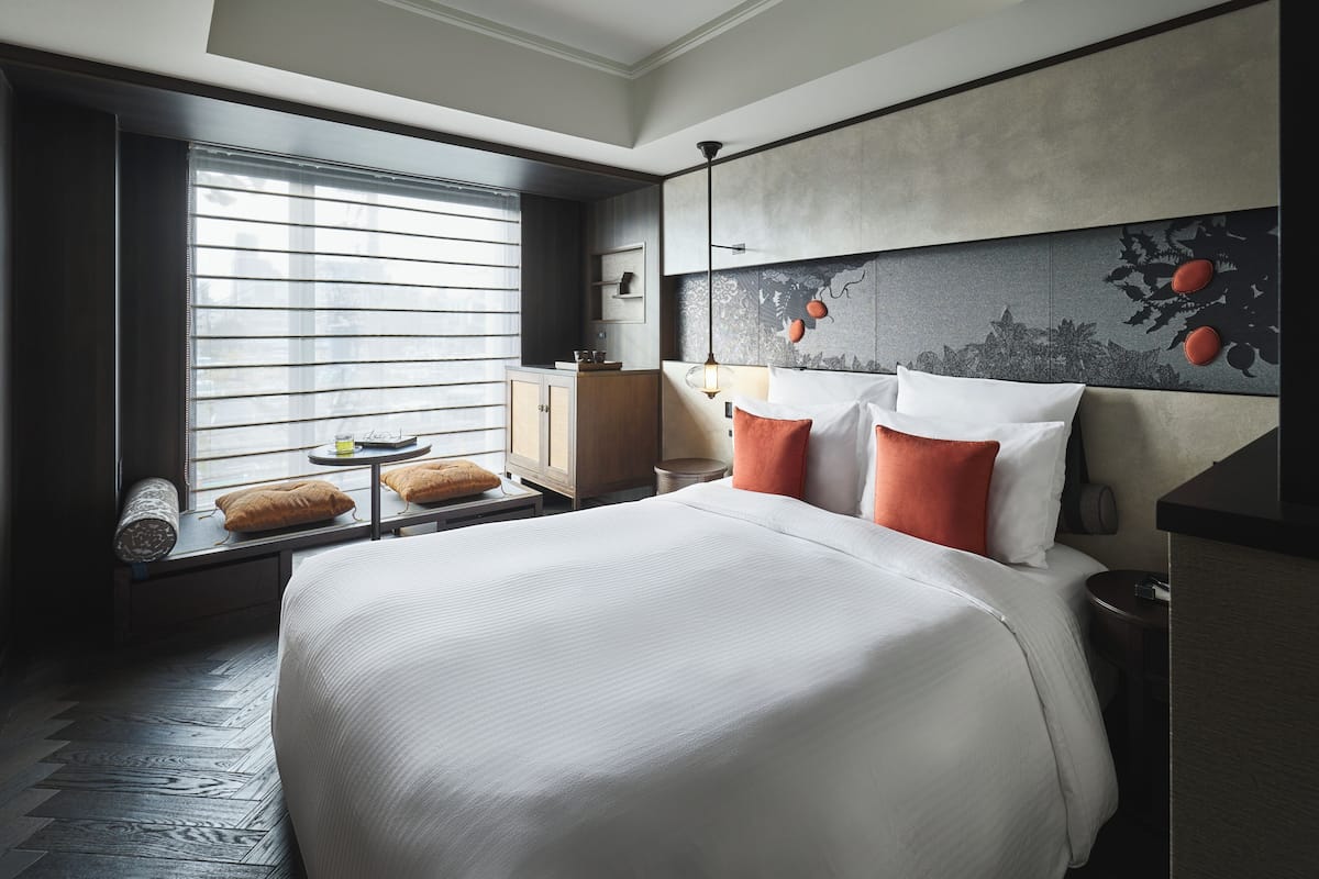 Ein Hotelzimmer mit einem großen Bett, einem Fenster mit Jalousien, einem Nachttisch und einem Kopfteil mit einem Zierpaneel.